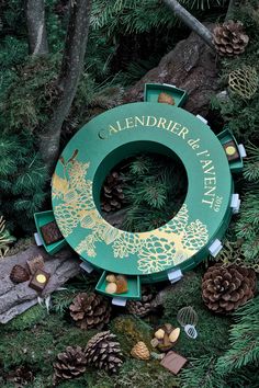 an overhead view of a green wreath surrounded by pine cones and evergreen needles with the words calender & haven written on it