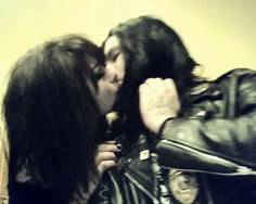 two women kissing each other in front of a wall with a leather jacket on it