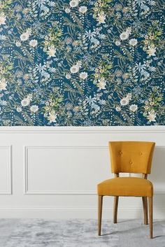 a yellow chair sitting in front of a blue wallpapered with white and green flowers