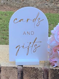 a sign that says cards and gifts next to a bouquet of flowers on a stone wall