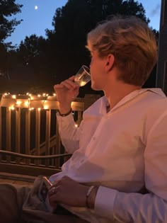 a man sitting on a porch drinking from a wine glass with lights in the background