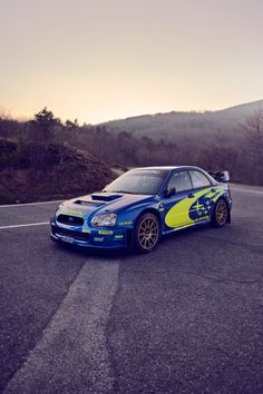 a blue and yellow car parked on the side of a road next to a mountain