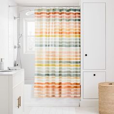 a bathroom with a shower curtain that has stripes on it and a basket in the corner