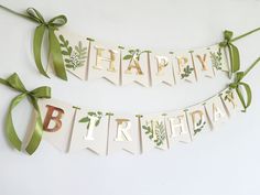 two happy birthday banners with green ribbons and bows on them, hanging from the wall