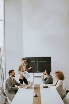 four people sitting at a table in front of a blackboard with notes on it