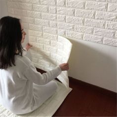 a woman sitting on top of a bed in front of a brick wall with white paint