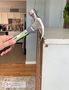 a person holding a wrench in their hand over a cabinet door that has been stripped off