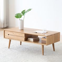 a wooden coffee table with a plant on top and books in the bottom drawer next to it