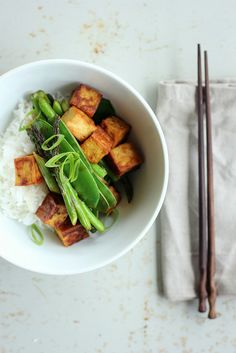 a white bowl filled with rice and vegetables next to chopsticks on a table