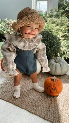 a small child in overalls and a hat standing on a rug next to pumpkins