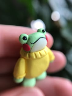 a small toy frog wearing a yellow shirt is held in the palm of someone's hand