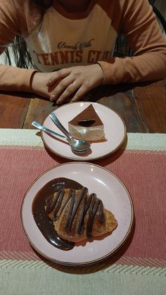 a woman sitting at a table with two plates of desserts on it and a fork in front of her