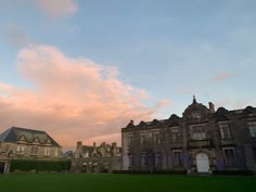 a large building sitting in the middle of a lush green field under a pink sky