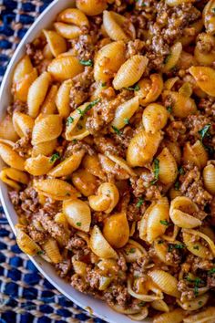 a white bowl filled with pasta covered in ground beef and sauce on top of a blue table cloth