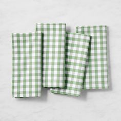 three green and white gingham napkins on a marble table top with one folded in