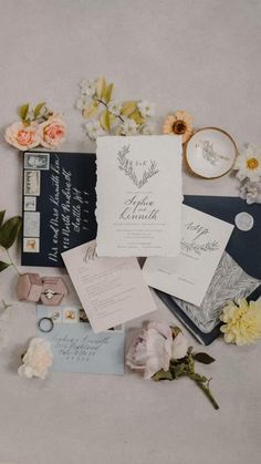 the wedding stationery is laid out on top of each other with flowers and rings