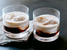 two glasses filled with ice on top of a table next to a napkin and spoon