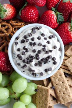 a white plate topped with fruit and crackers next to grapes, pretzels, strawberries and pretzels