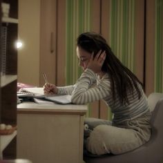 a woman sitting at a desk with a pen and notebook in front of her face