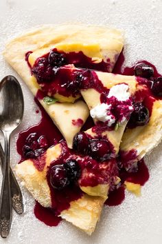 three slices of crepe with blueberry sauce and whipped cream on top next to a spoon