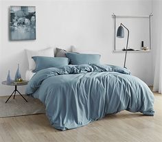 a bed with blue sheets and pillows in a white room next to a painting on the wall