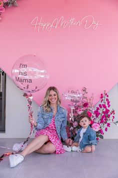 a woman and child sitting on the floor with balloons in front of a pink wall