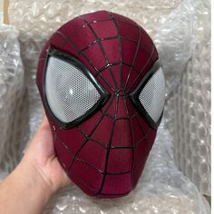 a spiderman mask is being held up by someone's hand