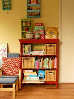 a red book shelf filled with lots of books next to a blue chair and yellow wall