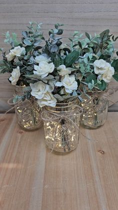 three glass jars with flowers and greenery in them sitting on a wooden table top