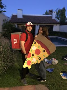 a man and woman standing in front of a house holding a large pizza shaped kite