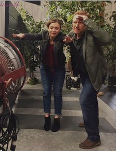 two people standing next to each other in front of an air conditioner and some plants