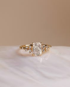 an engagement ring with three stones on top of white and gold marbles in front of a beige background