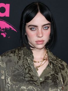 a close up of a person with black hair and blue eyes wearing a green shirt