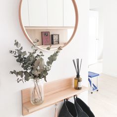 a round mirror hanging on the wall next to a shelf with flowers and plants in it