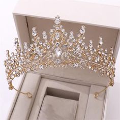 a gold tiara in a box with its lid open to show it's crystal stones