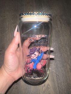 a hand holding a glass jar with an image of a cowboy on the bottom and words written in it