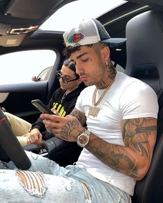 two young men sitting in the back seat of a car looking at their cell phones