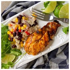 a white plate topped with chicken, rice and beans next to cilantro wedges