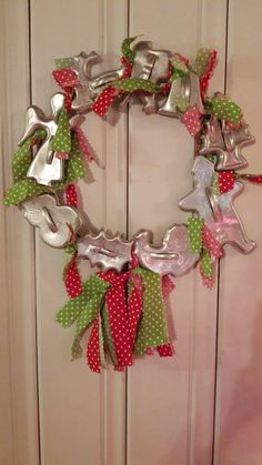 a christmas wreath made out of cookie cutters hanging on a door with green and red ribbons