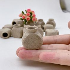 a hand is holding a small vase in front of some smaller clay pots and flowers