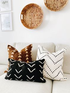 three woven baskets hang on the wall above a white couch with black and white pillows