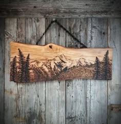 a wooden sign hanging on the side of a wall with mountains and trees painted on it