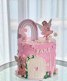 a pink birthday cake with fairy decorations on top