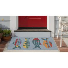 a door mat with fish on it in front of a red door and white chair