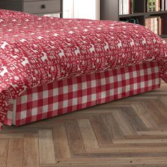 a red and white checkered bedspread on a bed with bookshelves in the background