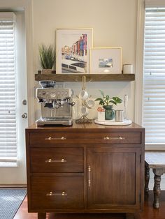 a coffee maker on top of a wooden cabinet in a room with white shutters