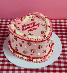 a heart shaped birthday cake sitting on top of a white plate with red checkered table cloth