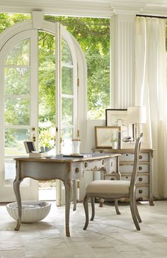 a white desk and chair in front of an open window with large arched glass doors