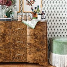 an old dresser with many bottles and glasses on it next to a wallpapered wall