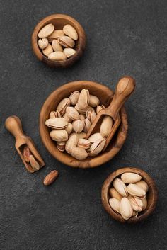 three wooden bowls filled with nuts on top of a black surface next to two spoons